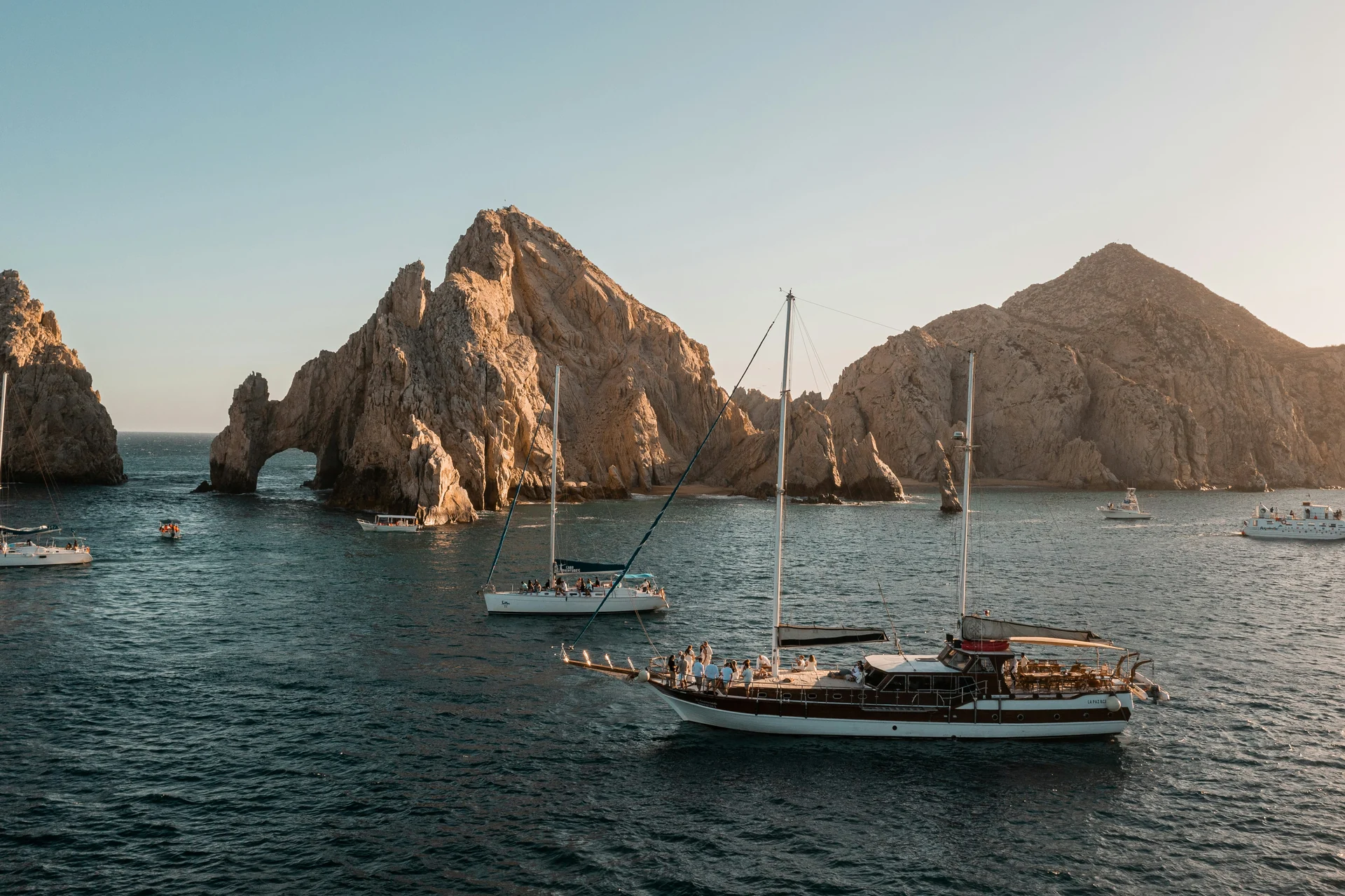 Tmavá dřevěná plachetnice zakotvená v zátoce u El Arco v Cabo San Lucas, osvětlená zapadajícím sluncem