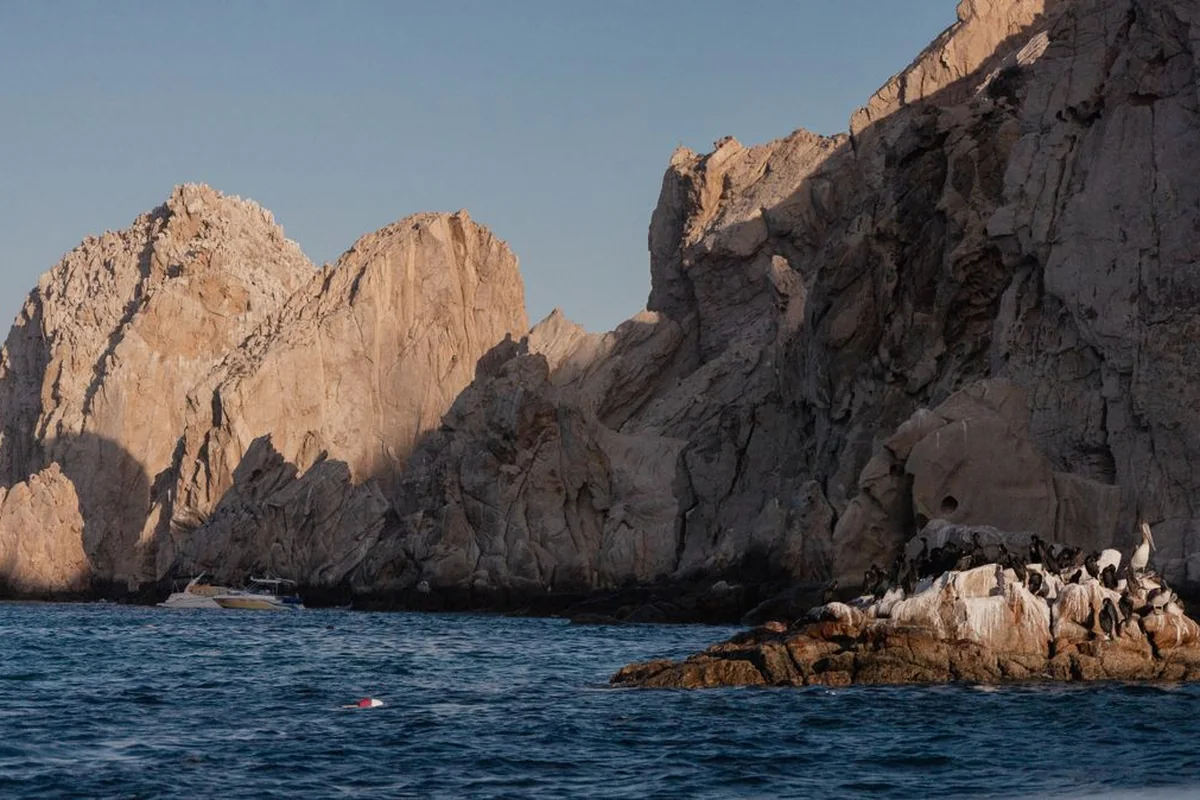 Žulové útesy Land's End v Cabo San Lucas, pod nimiž kotví malá loď a na skalách sedí mořští ptáci